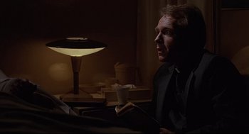 Movie still from “Psycho III” (1986), directed by Anthony Perkins – A man sitting in front of a lamp in a dark room; Close Up shot, Over the shoulder angle