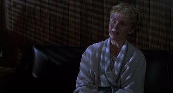 Movie still from “Psycho III” (1986), directed by Anthony Perkins – A woman sitting on a couch wearing a white robe; Medium shot, Over the shoulder angle
