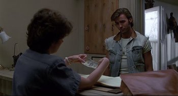Movie still from “Psycho III” (1986), directed by Anthony Perkins – A man in a jean jacket is holding money in front of a woman; Medium shot, Over the shoulder angle