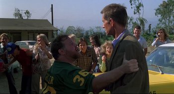 Movie still from “Psycho III” (1986), directed by Anthony Perkins – A man in a football jersey hugging another man in a suit; Medium shot, Over the shoulder angle