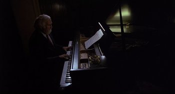 Movie still from “Psycho III” (1986), directed by Anthony Perkins – A man sitting at a piano in a dark room; Medium shot, High angle
