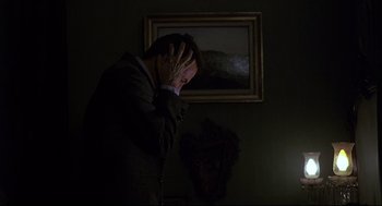 Movie still from “Psycho III” (1986), directed by Anthony Perkins – A man standing in a dark room holding his hands to his face; Close Up shot, Over the shoulder angle