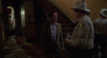 Movie still from “Psycho III” (1986), directed by Anthony Perkins – A man in a suit and tie standing next to a man in a sheriff's uniform; Medium shot, Over the shoulder angle