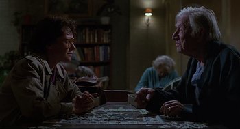 Movie still from “Psycho III” (1986), directed by Anthony Perkins – Two older people sitting at a table playing a puzzle; Medium shot, Over the shoulder angle