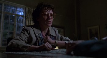 Movie still from “Psycho III” (1986), directed by Anthony Perkins – A woman sitting at a table in a dark room; Medium shot, Low angle