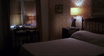 Movie still from “Psycho III” (1986), directed by Anthony Perkins – A bedroom with a bed , desk , lamp and a window; Wide shot, High angle