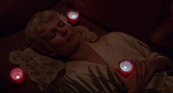 Movie still from “Psycho III” (1986), directed by Anthony Perkins – A woman laying on the ground with candles in her hands; Close Up shot, Overhead angle