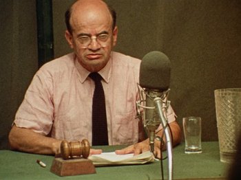 An older man sitting at a table in front of a microphone