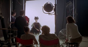 Movie still from “Puzzle of a Downfall Child” (1970), directed by Jerry Schatzberg – A group of people sitting in front of an image of a woman; Wide shot, Over the shoulder angle