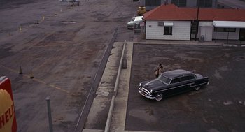 Movie still from “Puzzle of a Downfall Child” (1970), directed by Jerry Schatzberg – An old car parked in a parking lot next to a building; Extreme Wide shot, High angle