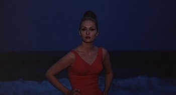 Movie still from “Puzzle of a Downfall Child” (1970), directed by Jerry Schatzberg – A woman in a red dress standing in front of a body of water at night; Medium shot, Low angle