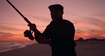Movie still from “Puzzle of a Downfall Child” (1970), directed by Jerry Schatzberg – A man holding a baseball bat on the beach; Medium shot, Low angle