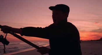 Movie still from “Puzzle of a Downfall Child” (1970), directed by Jerry Schatzberg – A man holding a baseball bat on the beach; Medium shot, Low angle