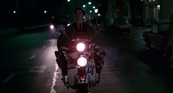 Movie still from “Quadrophenia” (1979), directed by Franc Roddam – A man riding a motorcycle down a street at night; Wide shot, Low angle