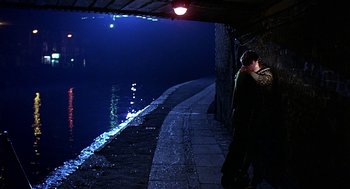 Movie still from “Quadrophenia” (1979), directed by Franc Roddam – A man standing next to a body of water at night; Wide shot, High angle