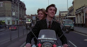 Movie still from “Quadrophenia” (1979), directed by Franc Roddam – A man and a woman riding a motorcycle down a street; Medium shot, Low angle