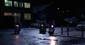 Movie still from “Quadrophenia” (1979), directed by Franc Roddam – A group of people riding motorcycles on a wet street at night; Wide shot, High angle