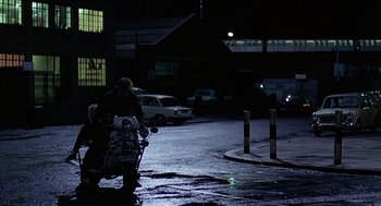 Movie still from “Quadrophenia” (1979), directed by Franc Roddam – A man riding a motorcycle down a street at night; Wide shot, Low angle