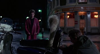 Movie still from “Quadrophenia” (1979), directed by Franc Roddam – A man standing next to a car on a street; Medium shot, Over the shoulder angle
