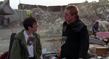 Movie still from “Quadrophenia” (1979), directed by Franc Roddam – Two young men are standing in a pile of garbage; Medium shot, Low angle