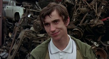 Movie still from “Quadrophenia” (1979), directed by Franc Roddam – A young man standing in front of a pile of car parts; Close Up shot, Over the shoulder angle