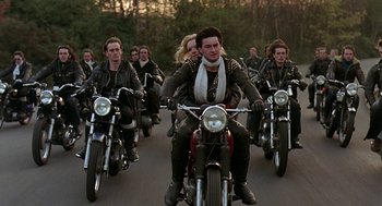Movie still from “Quadrophenia” (1979), directed by Franc Roddam – A group of people riding motorcycles down a street; Wide shot, High angle