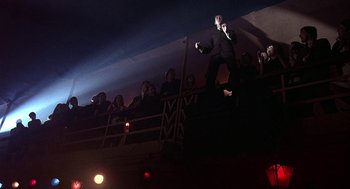 Movie still from “Quadrophenia” (1979), directed by Franc Roddam – A man in a black suit standing on top of a stage; Wide shot, Low angle