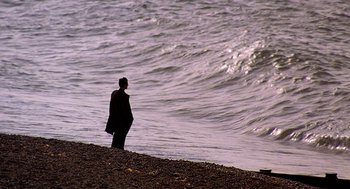 Movie still from “Quadrophenia” (1979), directed by Franc Roddam – A man standing on the beach looking out at the water; Extreme Wide shot, High angle