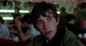 Movie still from “Quadrophenia” (1979), directed by Franc Roddam – A young man sitting at a table in front of a group of people; Close Up shot, Over the shoulder angle