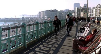 Movie still from “Quadrophenia” (1979), directed by Franc Roddam – Two people are walking on a bridge over a river; Wide shot, High angle