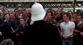 Movie still from “Quadrophenia” (1979), directed by Franc Roddam – A group of people standing in a crowd with a man wearing a white hat; Medium shot, Over the shoulder angle