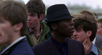 Movie still from “Quadrophenia” (1979), directed by Franc Roddam – A man in a suit and a hat is standing in front of other men; Close Up shot, Over the shoulder angle