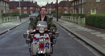 Movie still from “Quadrophenia” (1979), directed by Franc Roddam – A man riding on the back of a motorcycle down a street; Medium shot, Low angle