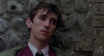Movie still from “Quadrophenia” (1979), directed by Franc Roddam – A man in a suit and tie standing in front of a stone wall; Close Up shot, Low angle
