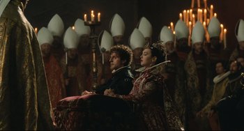 Movie still from “Queen Margot” (1994), directed by Patrice Chéreau – A couple of people that are sitting in front of a group; Wide shot, Over the shoulder angle