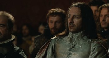 Movie still from “Queen Margot” (1994), directed by Patrice Chéreau – A man with long hair wearing a silver robe; Close Up shot, Over the shoulder angle