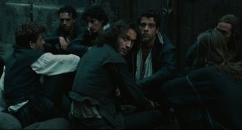 Movie still from “Queen Margot” (1994), directed by Patrice Chéreau – A group of men sitting next to each other in a dark room; Medium shot, High angle