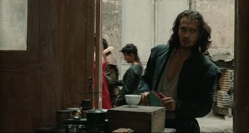 Movie still from “Queen Margot” (1994), directed by Patrice Chéreau – A man standing next to a table with a cup of coffee; Medium shot, Over the shoulder angle