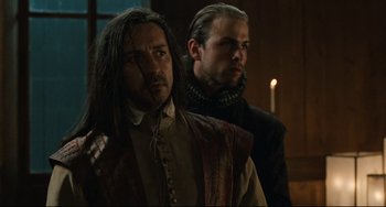 Movie still from “Queen Margot” (1994), directed by Patrice Chéreau – A man with long black hair standing next to another man with blond hair; Medium shot, Over the shoulder angle