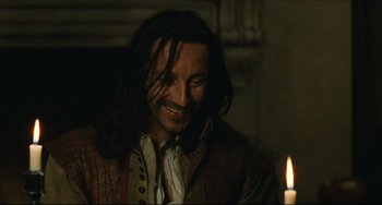 Movie still from “Queen Margot” (1994), directed by Patrice Chéreau – A man with long black hair is smiling at a candle; Close Up shot, Over the shoulder angle
