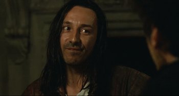 Movie still from “Queen Margot” (1994), directed by Patrice Chéreau – A man with long black hair is smiling for the camera; Close Up shot, Over the shoulder angle