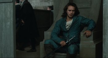 Movie still from “Queen Margot” (1994), directed by Patrice Chéreau – A man sitting in a chair holding a sword in his hand; Medium shot, High angle