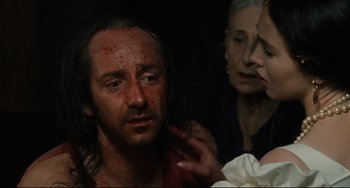 Movie still from “Queen Margot” (1994), directed by Patrice Chéreau – A man with blood all over his face is being examined by two women; Close Up shot, Over the shoulder angle