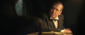 Movie still from “Queen of the Desert” (2015), directed by Werner Herzog – An older man sitting at a table in front of papers; Close Up shot, Over the shoulder angle