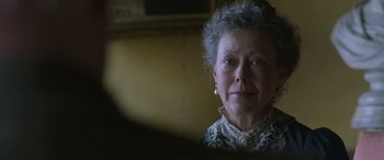Movie still from “Queen of the Desert” (2015), directed by Werner Herzog – An older woman wearing a white dress and pearls; Close Up shot, Over the shoulder angle