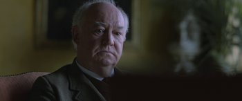 Movie still from “Queen of the Desert” (2015), directed by Werner Herzog – An older man wearing a suit and tie; Close Up shot, Over the shoulder angle