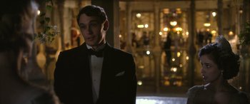 Movie still from “Queen of the Desert” (2015), directed by Werner Herzog – A man in a tuxedo standing in front of a building at night; Medium shot, Over the shoulder angle
