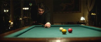 Movie still from “Queen of the Desert” (2015), directed by Werner Herzog – A man is playing a game of billiards on a pool table; Medium shot, Over the shoulder angle