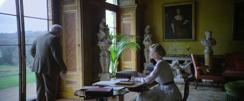 Movie still from “Queen of the Desert” (2015), directed by Werner Herzog – A woman sitting at a table writing on a piece of paper; Wide shot, Over the shoulder angle