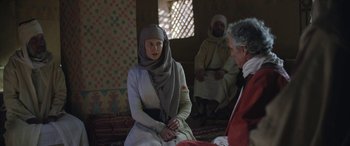 Movie still from “Queen of the Desert” (2015), directed by Werner Herzog – A woman wearing a headscarf sitting on a couch; Medium shot, Over the shoulder angle